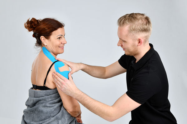 Physiotherapeut bringt Kinesiotape an der Schulter einer Patientin an